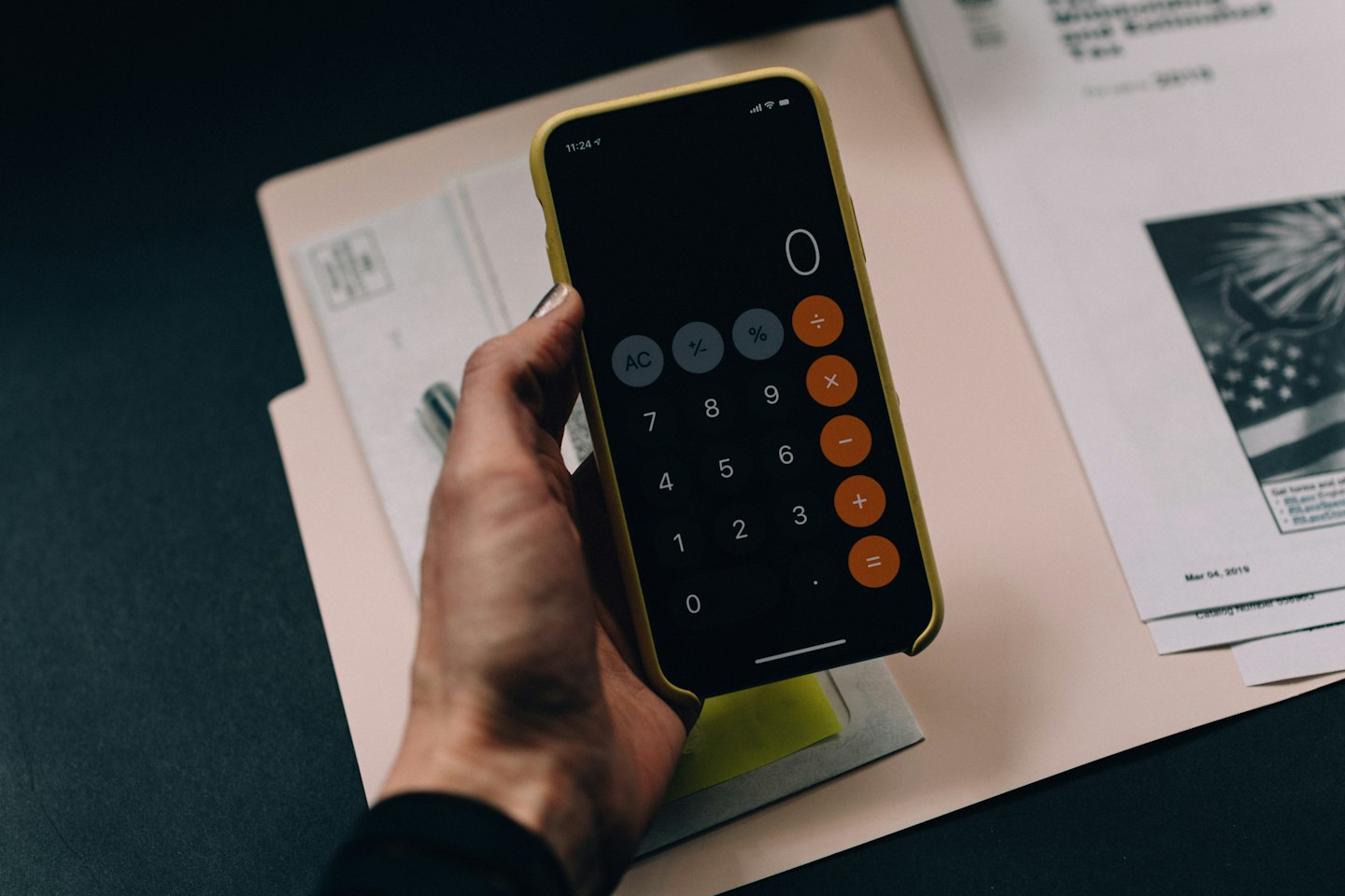 Hand holding a smartphone calculator above printed documents