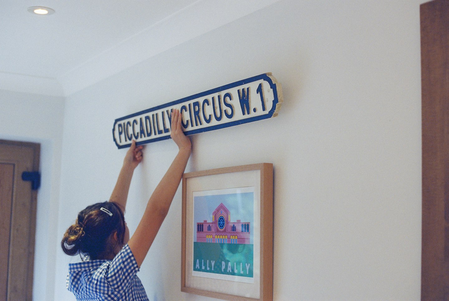 A person holding a vintage Piccadilly Circus street sign against a white wall